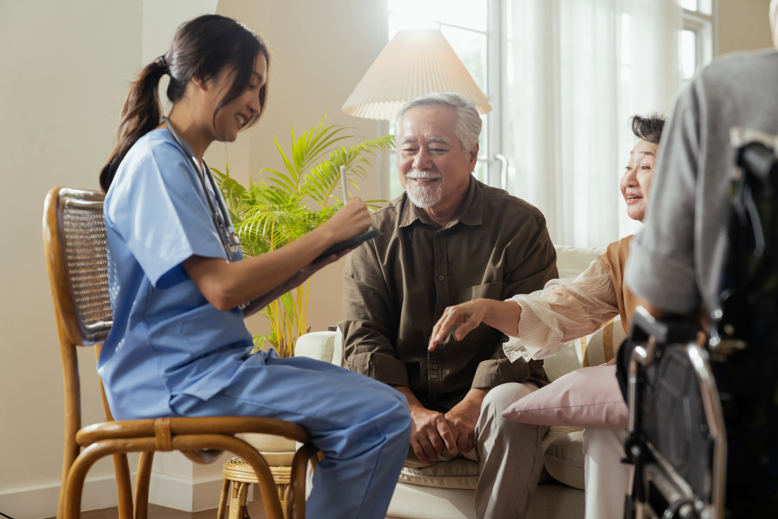 happiness Cheerful elderly woman and men talking with female caregiver nurse doctor having health checking consult at living area,Caretakers with senior couple sitting in living room at nursing home